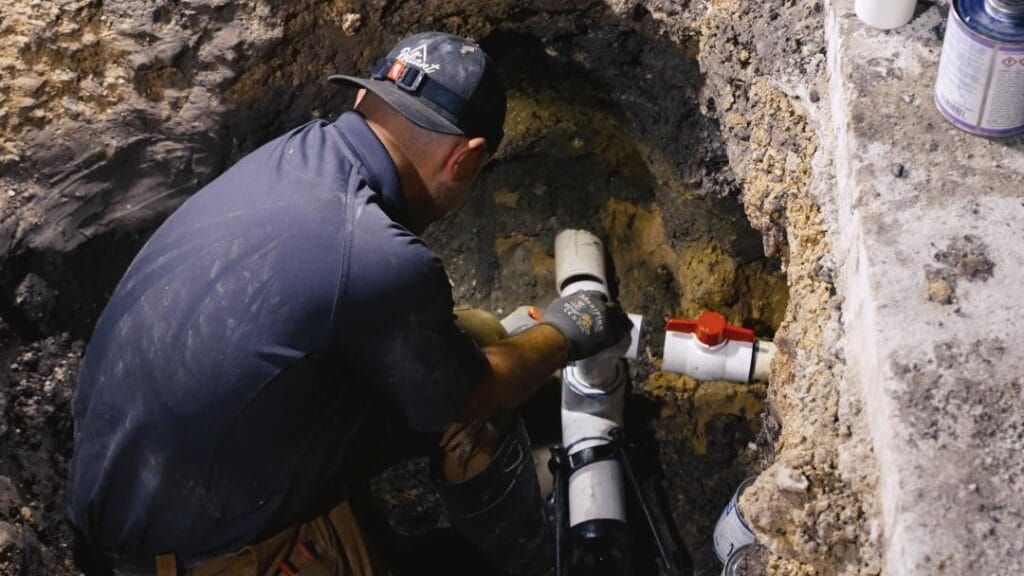 Plumber repairing an exposed pipe in an excavated trench