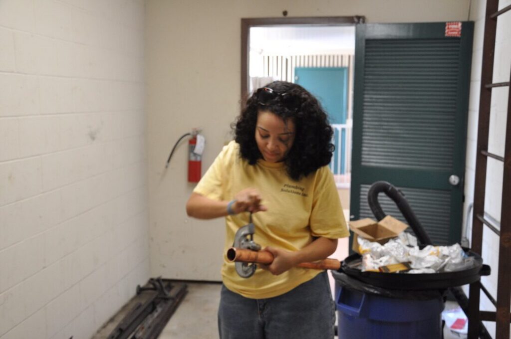 Plumber inspecting a fitting beside a bin of plumbing supplies