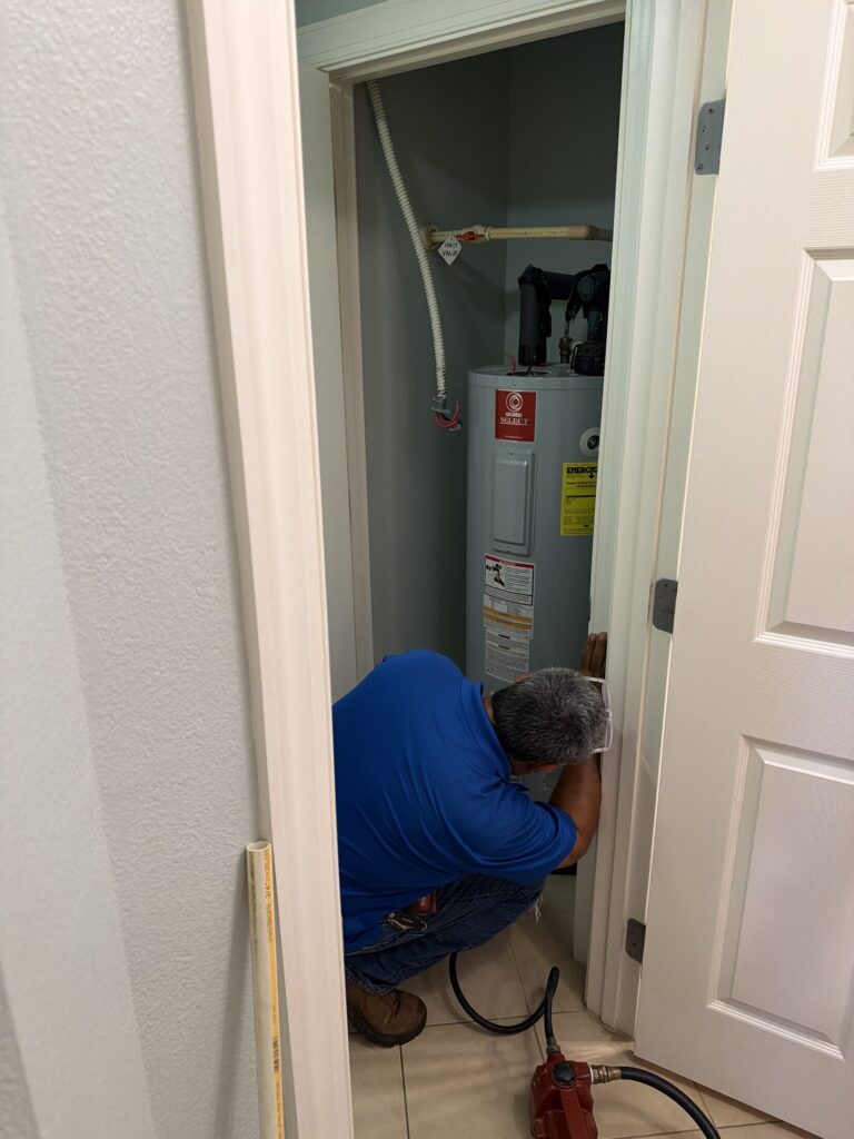 Plumber working on a water heater inside a utility closet