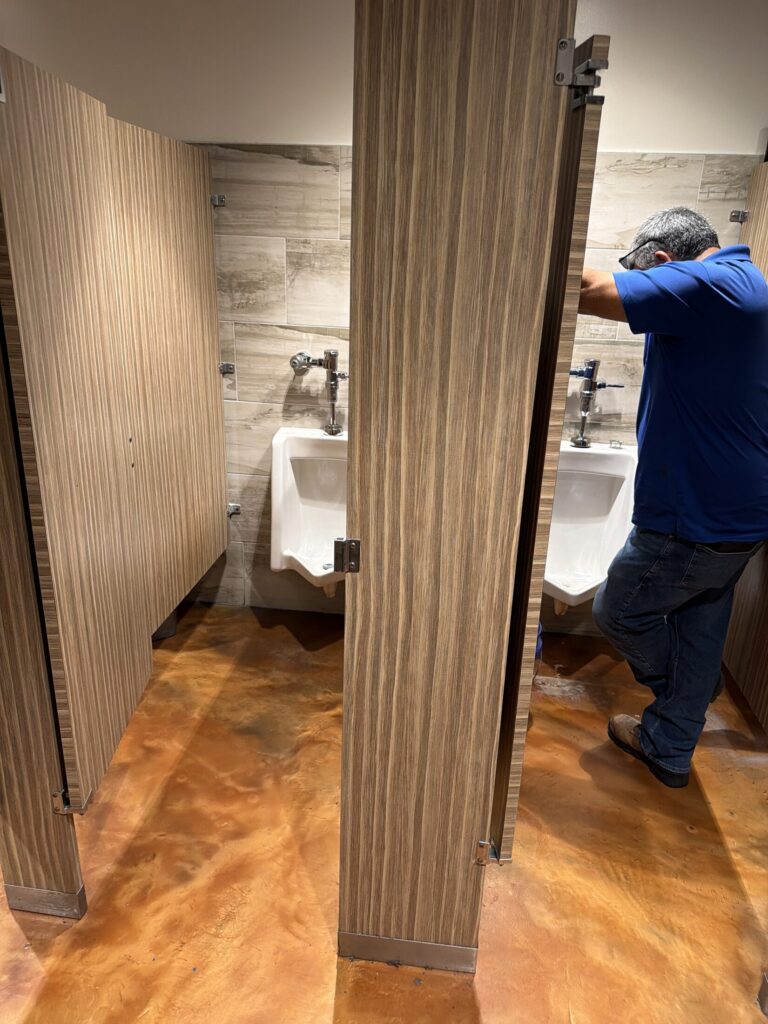 Plumber repairing restroom plumbing behind a stall partition