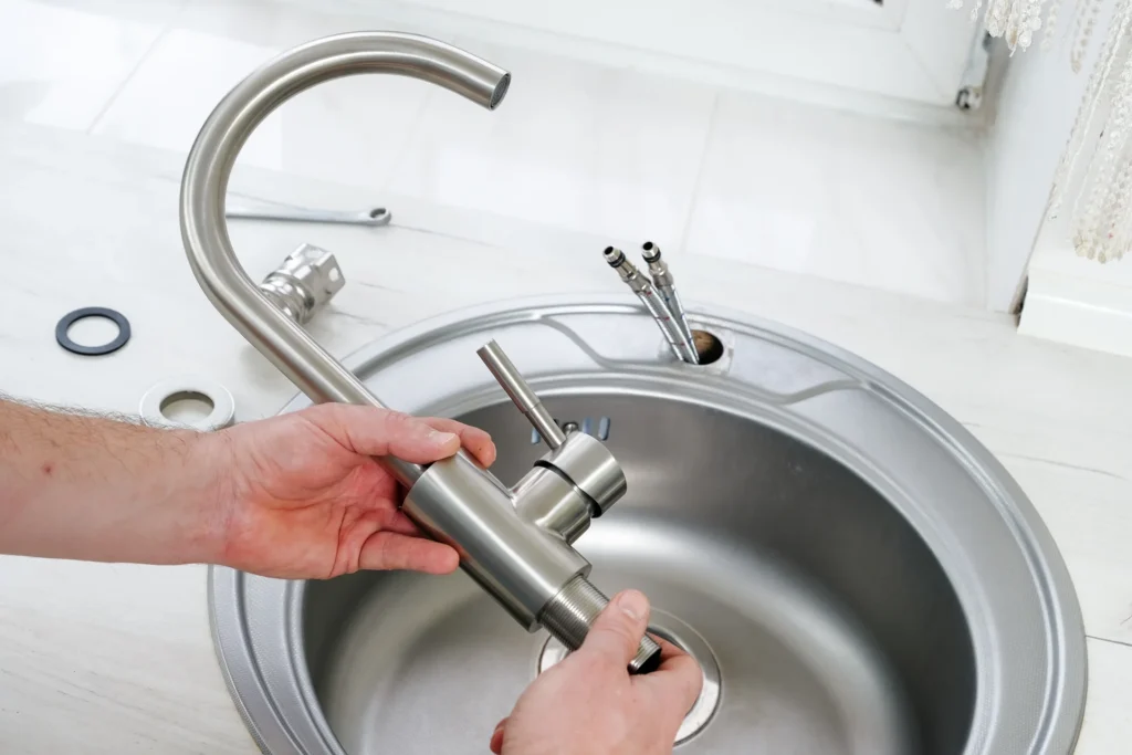 Hands installing a stainless steel kitchen faucet on a sink