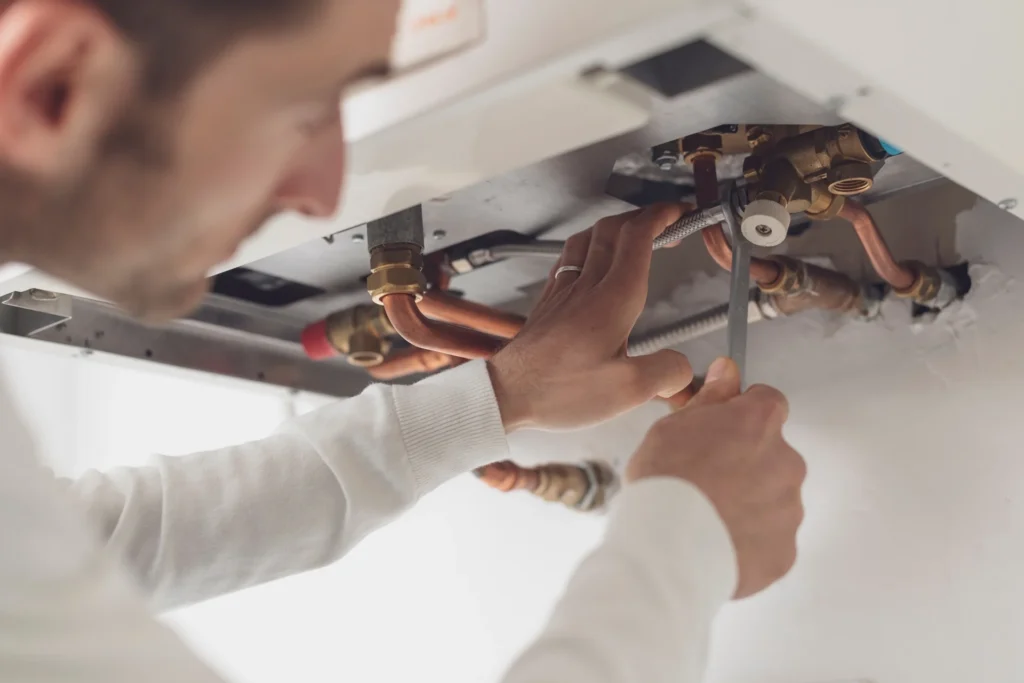 Plumber connecting pipe fittings beneath a wall-mounted unit