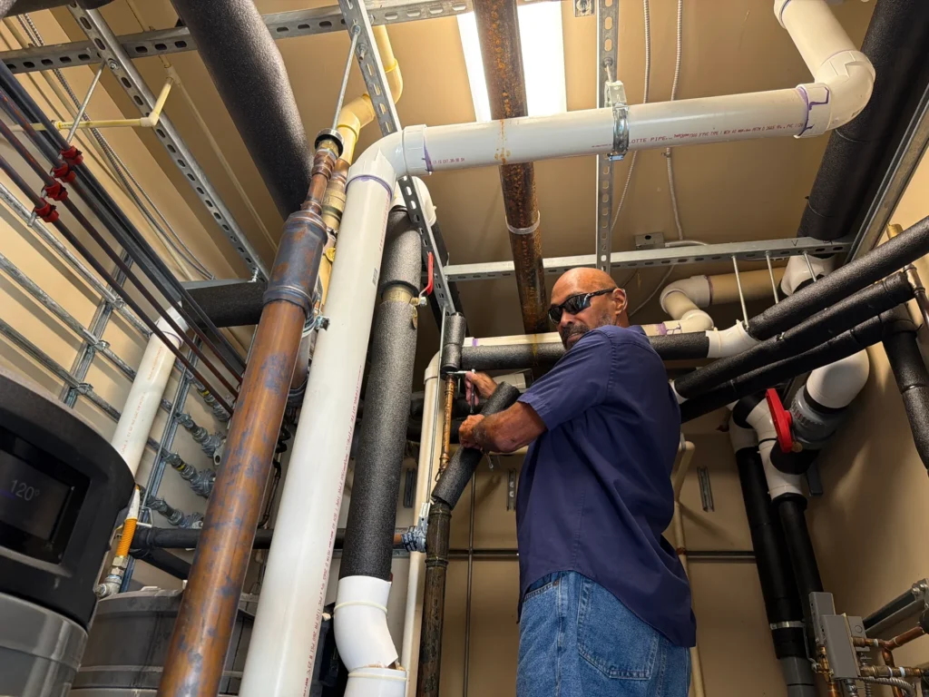 Plumber working on overhead water pipes in a mechanical room
