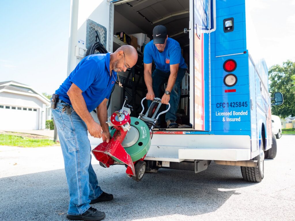 Plumbing technicians unloading a drain cleaning machine from a service van