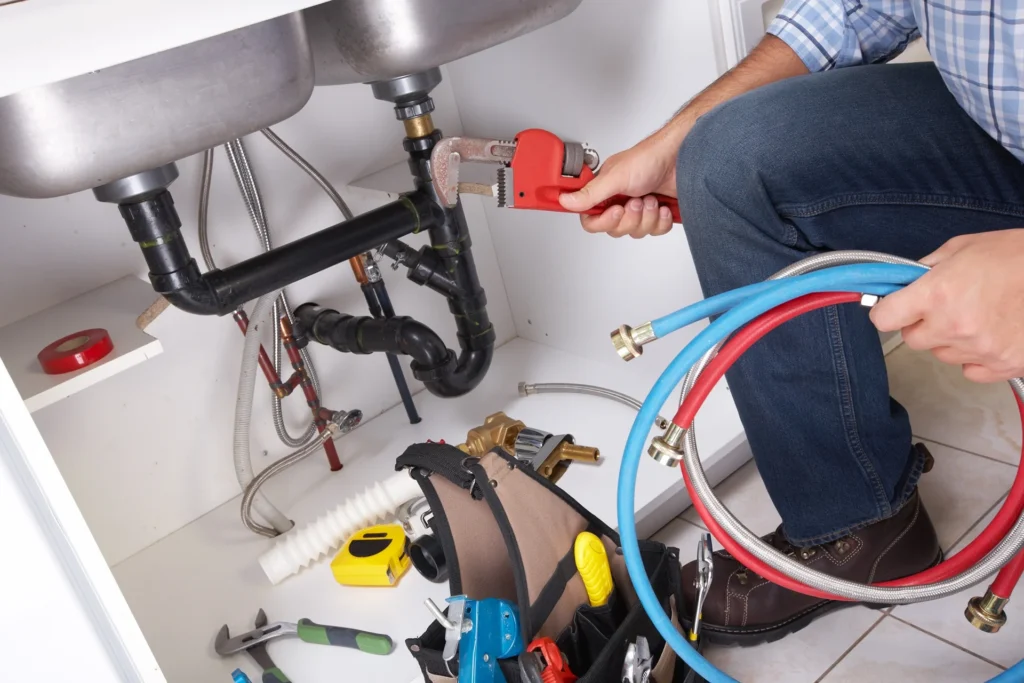 Plumber using a pipe wrench on under-sink plumbing with tools nearby
