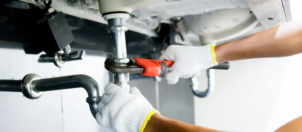 Gloved hands tightening a sink drain pipe with a wrench